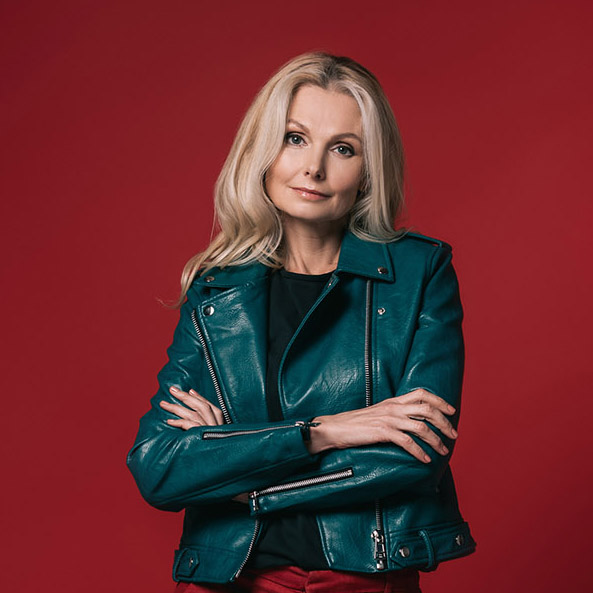 Editorial nature photography of mature blonde woman in green jacket with red background.